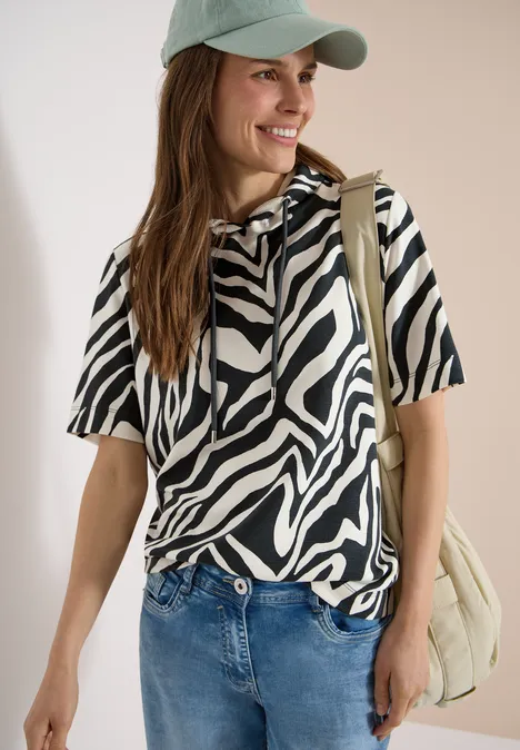Persoon met onscherp gezicht draagt zebra-t-shirt, jeans, pet en een lichte schoudertas.