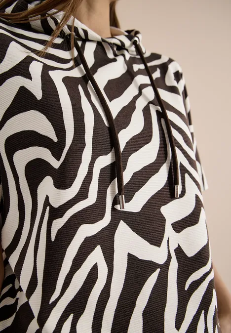 Close-up van een trui met zwart-wit zebrapatroon, capuchon en zichtbare koorden.