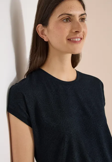 Shirt met burn-out look universal blue Jonge vrouw met halflang donker haar draagt een eenvoudig zwart shirt en glimlacht subtiel.