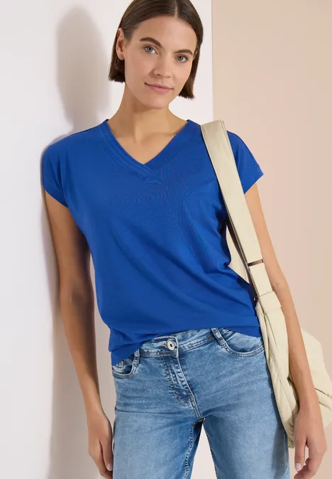 Frau trägt blaues V-T-Shirt, Jeans und eine helle Umhängetasche.