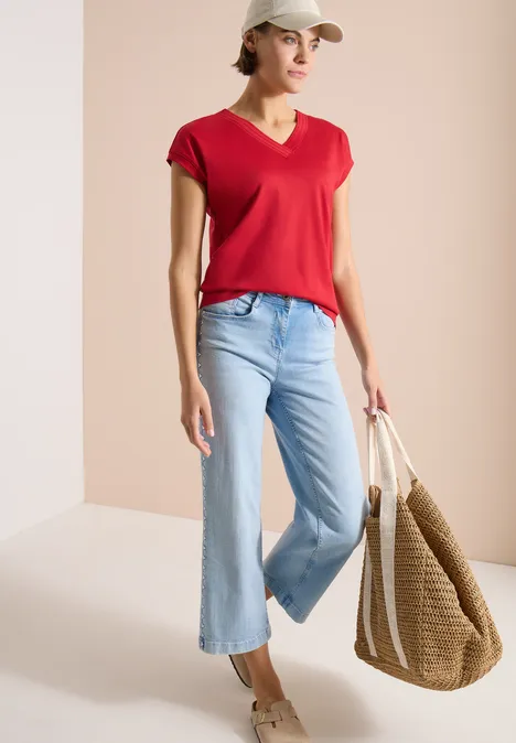 Vrouw draagt een rood T-shirt, wijde blauwe jeans en houdt een grote strooien tas.