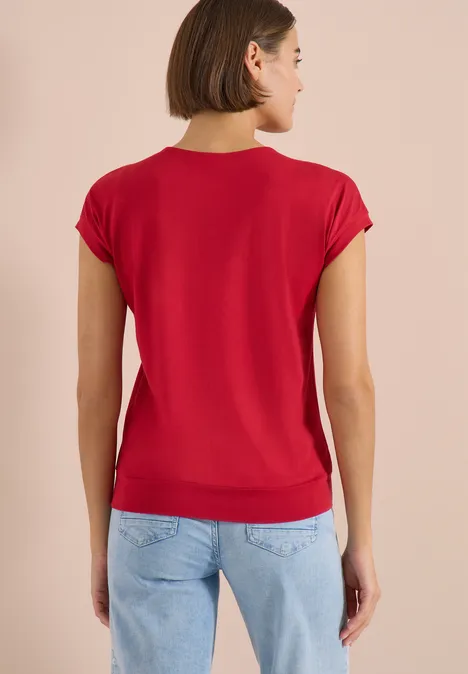 Vrouw van achteren in een rood T-shirt en lichtblauwe spijkerbroek voor een beige achtergrond