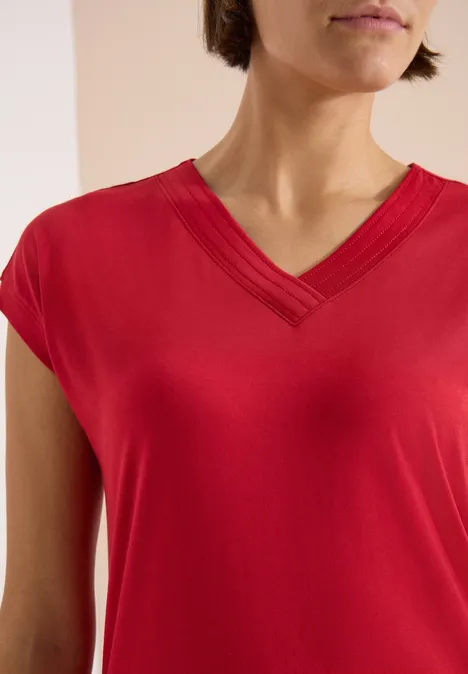 Close-up van een persoon in een rood V-hals T-shirt, zicht op schouders en borst.
