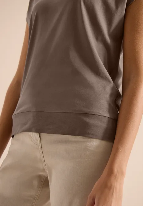 Shirt met korte mouwen en V-hals in effen kleur urban taupe Close-up van een bruin mouwloos shirt en beige broek, met focus op taille en armen.