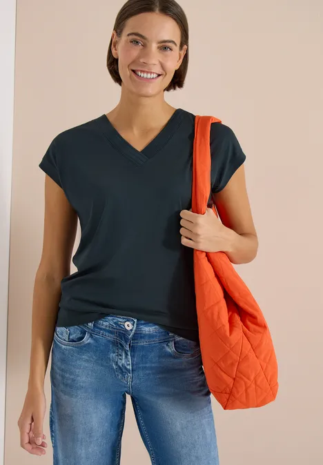 Shirt met korte mouwen en V-hals in effen kleur deep petrol blue Vrouw draagt donkerblauw V-hals T-shirt en jeans, met een oranje gewatteerde tas.
