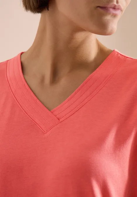Close-up van een koraalroze T-shirt met V-hals.