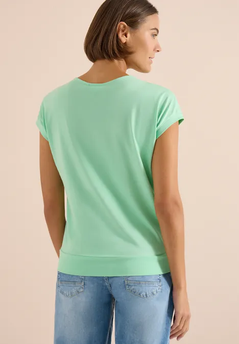 Shirt met korte mouwen en V-hals in effen kleur juicy lime Achteraanzicht van een persoon met lichtgroen T-shirt en spijkerbroek voor een lichte achtergrond.