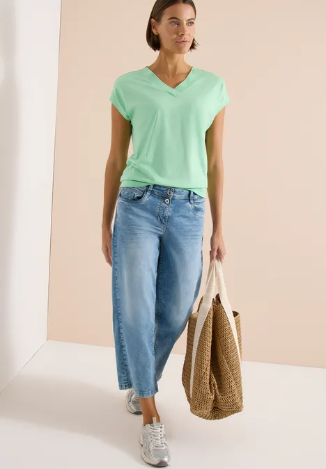 Shirt met korte mouwen en V-hals in effen kleur juicy lime Vrouw in mintgroen V-hals T-shirt, wijde cropped jeans, sneakers en stro shopper.