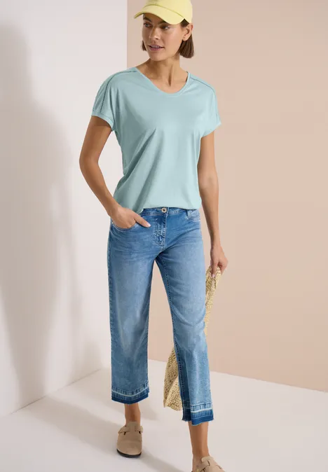 Shirt met V-hals en kanten detail crystal mint Vrouw draagt lichtturquoise V-hals T-shirt, losse blauwe jeans en beige loafers voor neutrale achtergrond.