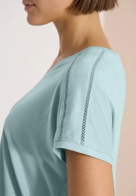 Shirt met V-hals en kanten detail crystal mint Zijaanzicht van een vrouw in pastelgroen T-shirt met sierstrepen, tegen een lichte achtergrond.