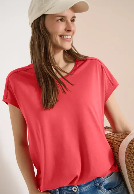 T-Shirt mit V-Neck und Spitzendetail coral Frau in rotem T-Shirt und Jeans, mit heller Kappe und Strohtasche