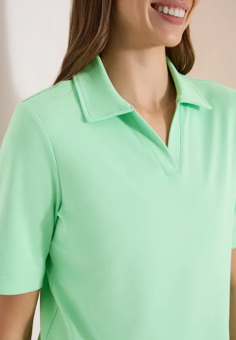 Een vrouw lacht en draagt een lichtgroen poloshirt met korte mouwen.