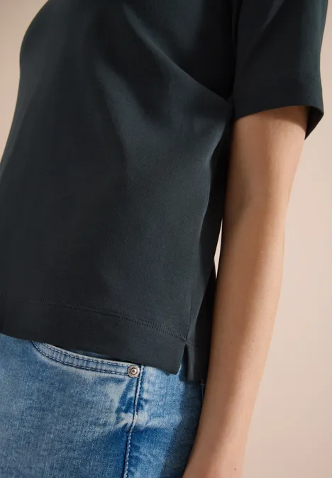 Zijaanzicht van een bovenlichaam in donkergroene T-shirt met korte mouwen en blauwe spijkerbroek.