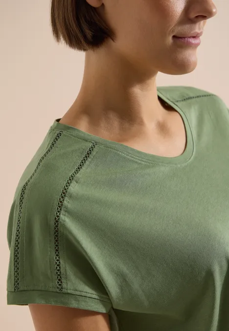 Nahaufnahme einer Frau in olivgrünem T-Shirt mit dekorativer Nahtverzierung an der Schulter.
