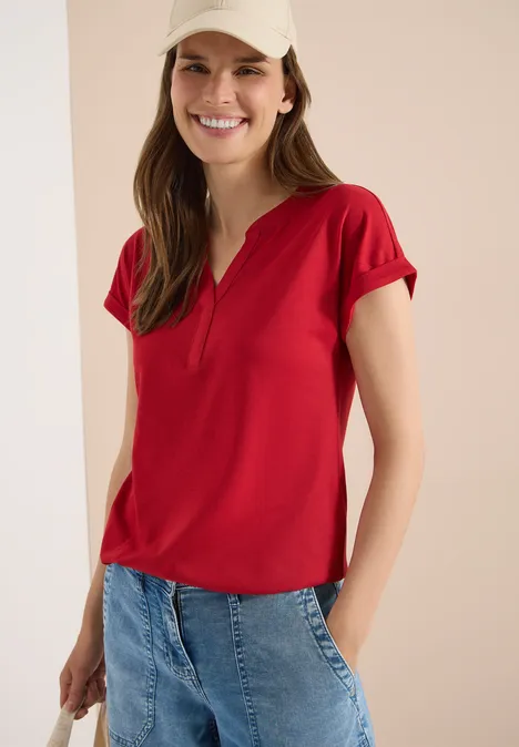 Kurzarm Shirt im Tunika-Look tamarillo red Frau trägt rotes Kurzarmshirt mit V-Ausschnitt und blaue Jeans vor einfarbig hellem Hintergrund.