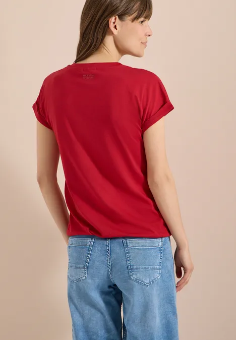 Kurzarm Shirt im Tunika-Look tamarillo red Frau steht Rücken zur Kamera und trägt rotes T-Shirt sowie blaue Jeans.
