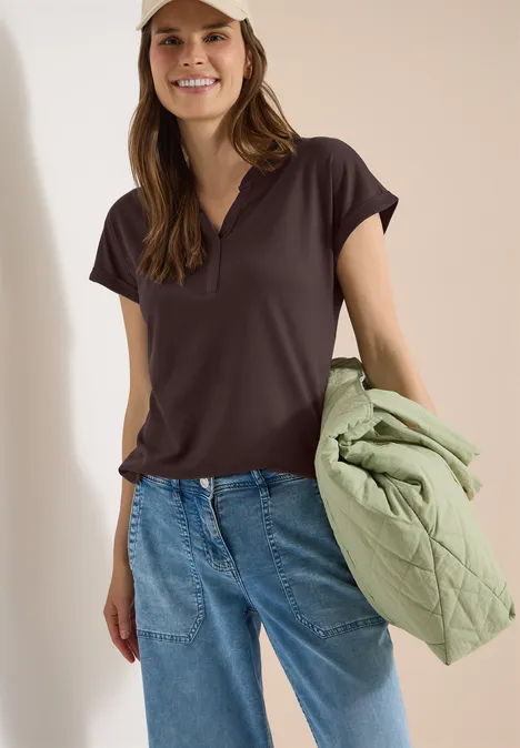 Kurzarm Shirt im Tunika-Look brown cacao Frau in dunklem T-Shirt und Jeans, hält eine hellgrüne gesteppte Jacke.