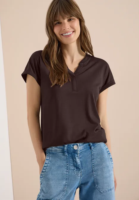 Kurzarm Shirt im Tunika-Look brown cacao Frau in schwarzem Poloshirt und blauen Jeans vor hellem Hintergrund.