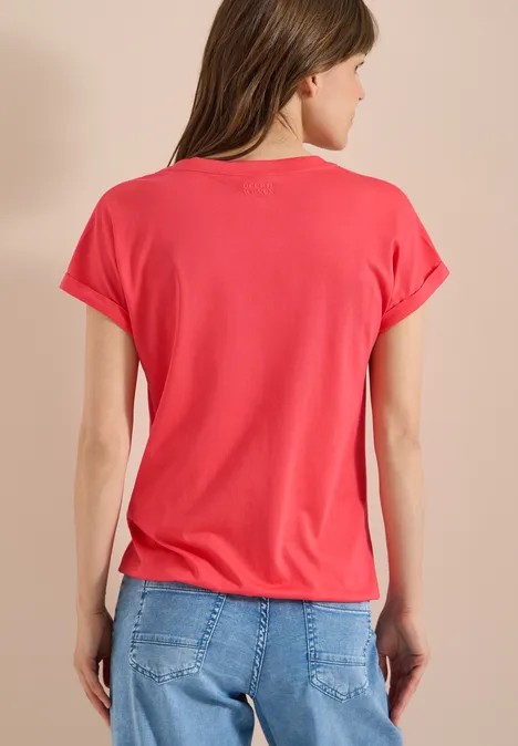 Kurzarm Shirt im Tunika-Look coral Frau von hinten in rotem T-Shirt und blauen Jeans vor beigem Hintergrund.