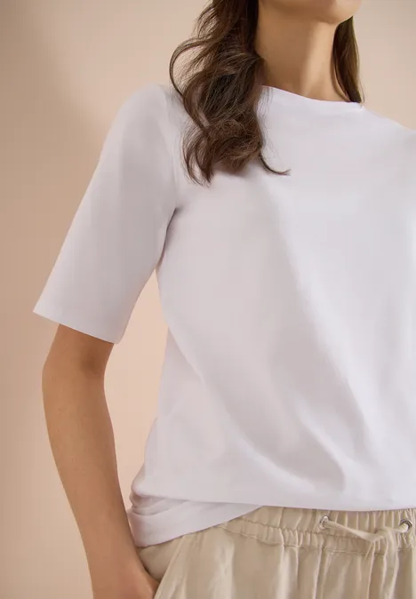 Basic Shirt met boothals White Vrouw met een wit T-shirt en comfortabele lichte broek voor een neutrale achtergrond