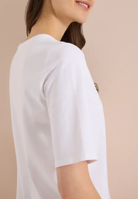 Basic Shirt met boothals White Zijaanzicht van een simpele witte t-shirt met halflange mouwen bij een vrouw voor een beige achtergrond.