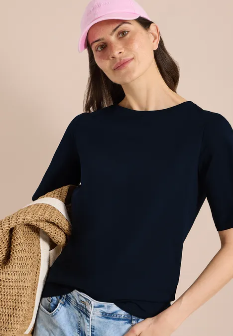 Basic Shirt met boothals universal blue Vrouw in marineblauw T-shirt met korte mouw en jeans draagt een strooien tas.