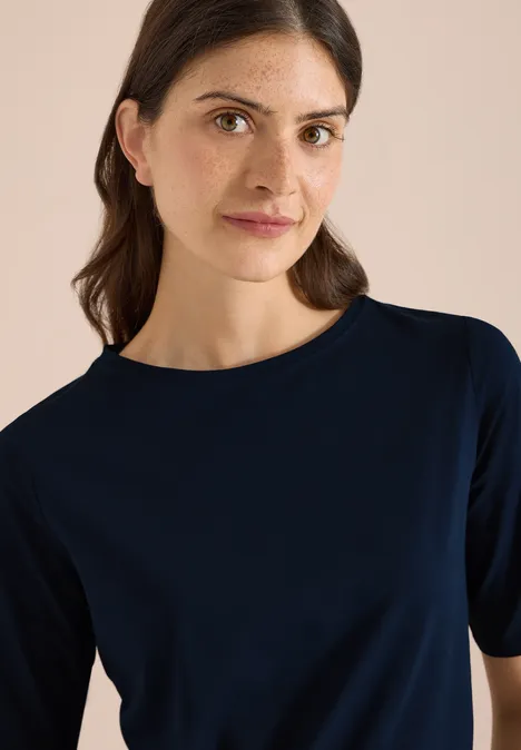 Basic Shirt met boothals universal blue Persoon met een donkerblauw T-shirt met korte mouwen voor een lichte achtergrond, gezicht vervaagd.