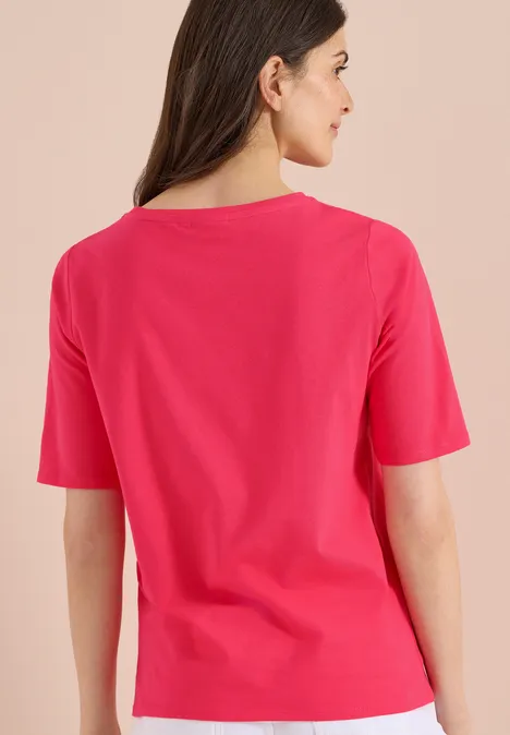 Basic Shirt met boothals geranium red Rugaanzicht van een vrouw met lang bruin haar in een roze T-shirt tegen een lichte achtergrond.