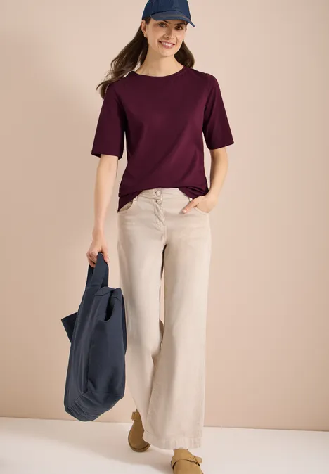 Basic Shirt met boothals sweet grape red Vrouw in paars T-shirt en beige palazzo-broek met een donkerblauwe tas voor een eenvoudige achtergrond.