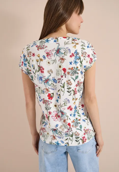 Frau von hinten in weißem Shirt mit buntem Blumenmuster und blauen Jeans.
