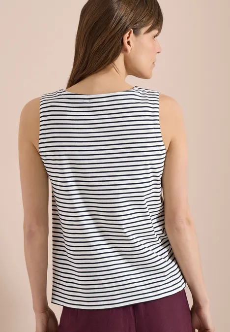 Kobieta tyłem w paskowanej, bezrękawnikowej bluzce na neutralnym tle.