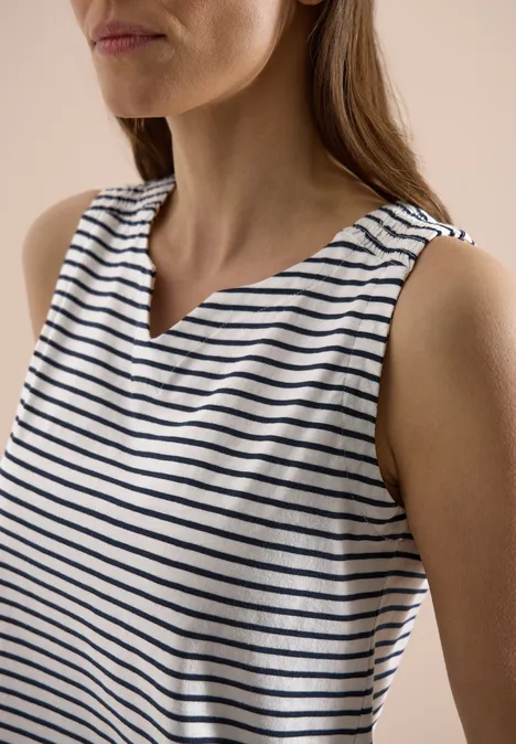 Kobieta w bezrękawniku w biało-niebieskie paski z subtelnym dekoltem w serek.