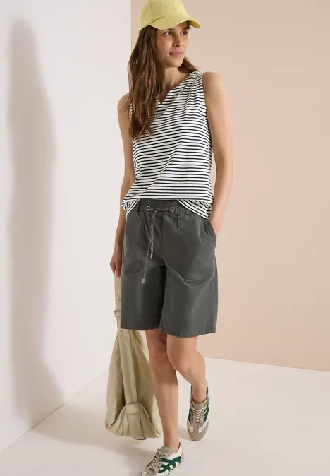 Personne porte un top rayé, un short bermuda ample, des sandales et une casquette sur fond clair.