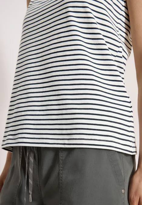 Femme porte un débardeur blanc à rayures bleues et un pantalon gris à cordon