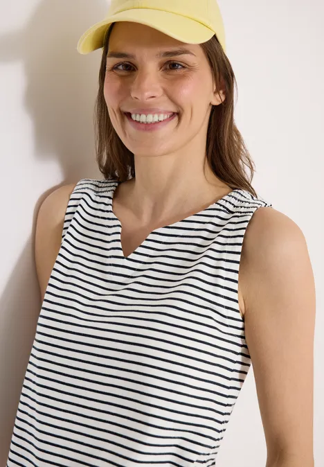 Personne portant un haut à rayures et un chapeau jaune devant un mur clair.