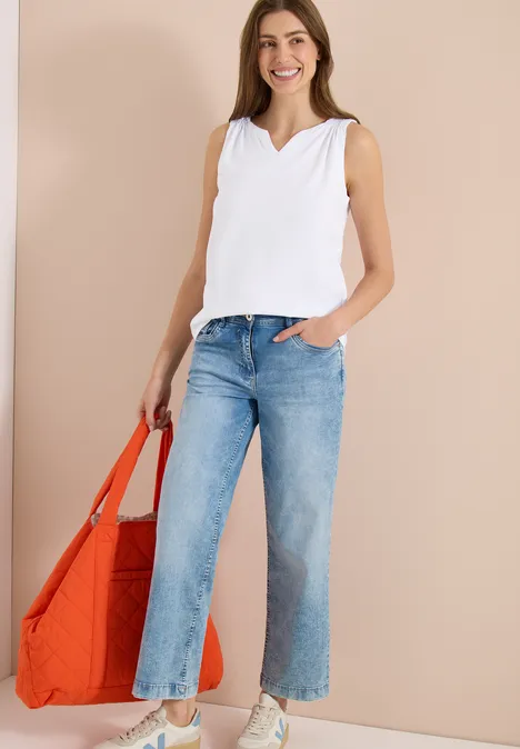 Vrouw in wit topje en lichtblauwe jeans met grote oranje tas voor een neutrale achtergrond.