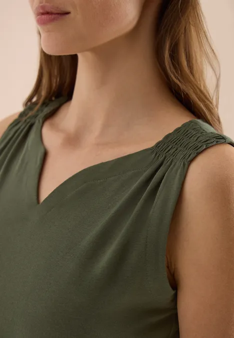 Vrouw in olijfgroene mouwloze top met V-hals en geplooide schouderbanden.