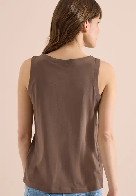 Een vrouw staat met de rug naar de camera en draagt een bruin mouwloos hemd.