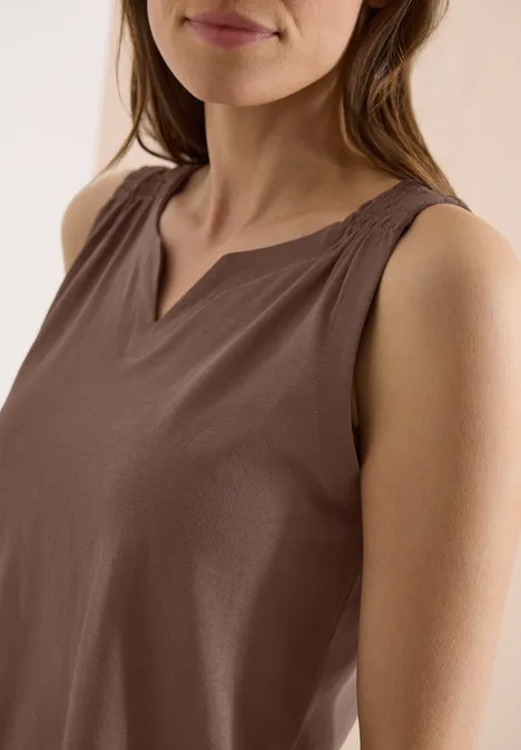 Vrouw met een mouwloze bruine top met V-hals.