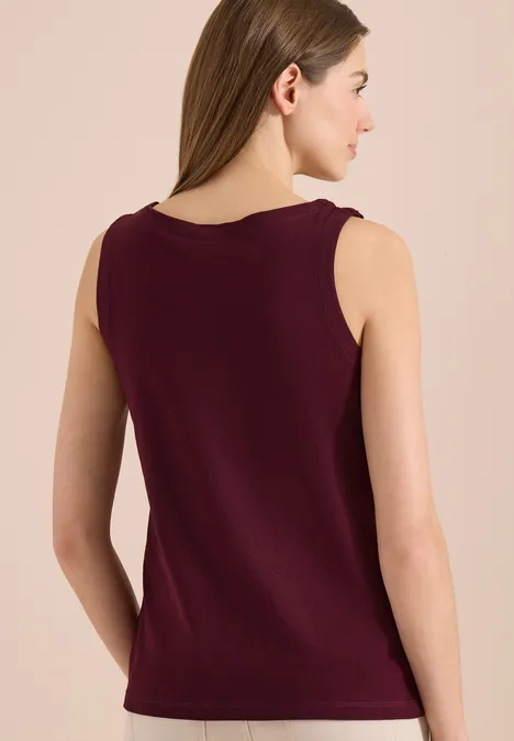 Vrouw van achteren in mouwloze bordeauxrode top tegen beige achtergrond