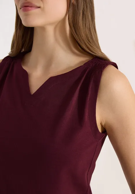 Een vrouw draagt een mouwloze bordeauxrode top met een subtiele V-vormige halsuitsnijding.