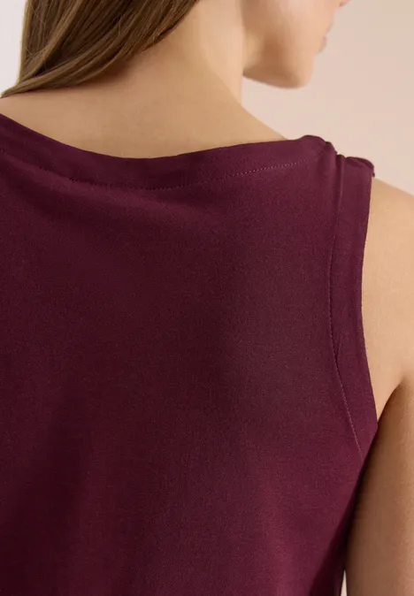 Rugaanzicht van vrouw met mouwloos top in bordeauxkleur