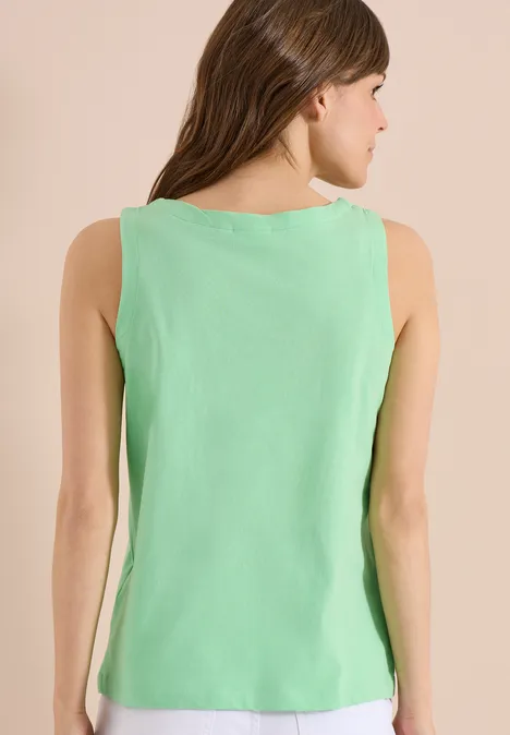 Rugaanzicht van een vrouw in een lichtgroen mouwloos topje tegen een beige achtergrond