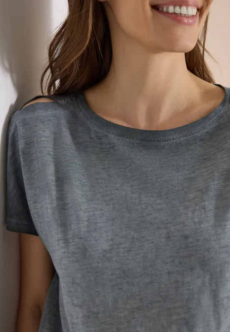 Vrouw leunt glimlachend in grijs t-shirt tegen muur, alleen bovenlichaam zichtbaar