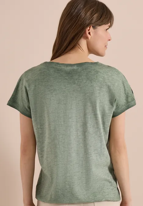 Vrouw van achteren in groen T-shirt met korte mouwen tegen effen achtergrond.