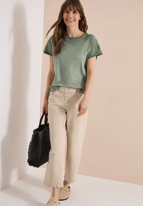 Vrouw in groen shirt en beige broek met een zwarte draagtas.