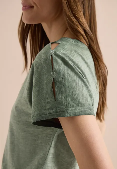 Zijaanzicht van een vrouw in een groen T-shirt met korte mouwen en schouderuitsnijdingen.