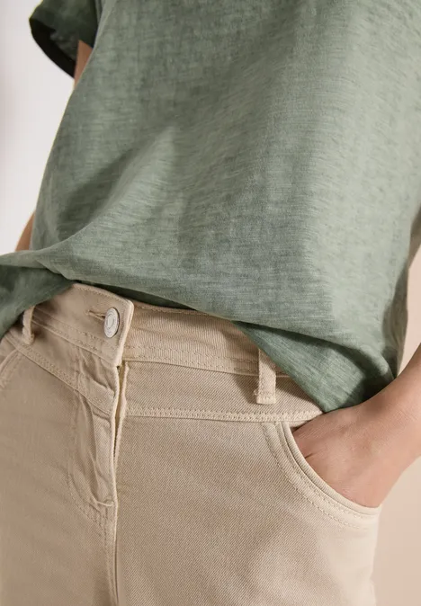 Iemand draagt een groen T-shirt en een beige broek met hoge taille, hand in de voorzak.