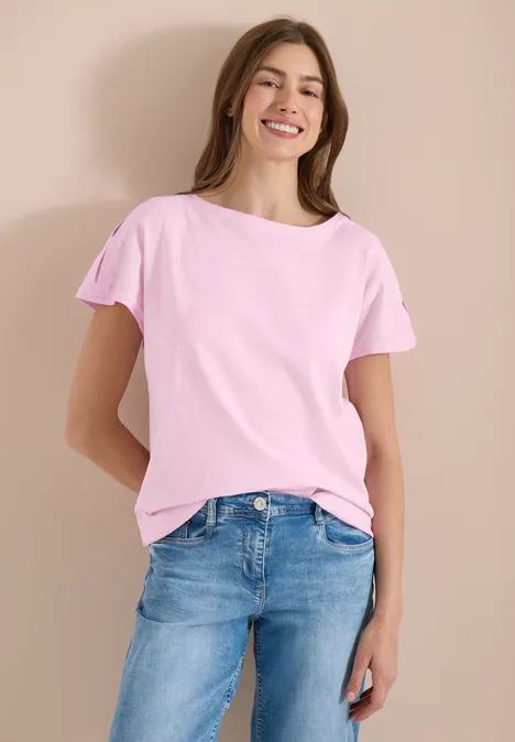 Junges Mädchen in rosa T-Shirt und blauen Jeans vor neutralem Hintergrund.