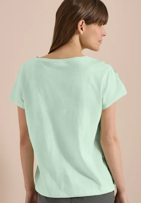 Rückenansicht einer Frau im mintgrünen T-Shirt vor einfarbigem Hintergrund.